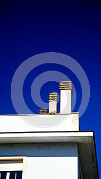 Three stone chimneys of different heights on a white building roof with blue sky in the background