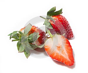 Three strawberries, one half and two whole ones behind it, are isolated on a white background