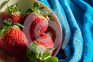 Three strawberries and sugar cane on blue cloth background in white bowl