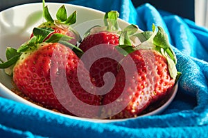 Three strawberries and sugar cane on blue cloth background in white bowl