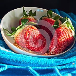 Three strawberries and sugar cane on blue cloth background in white bowl