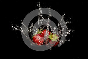 three strawberries with water splash on black background