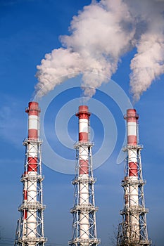 Three striped industrial pipes with smoke over cloudless blue sky