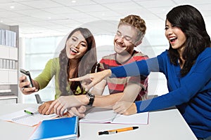 Three students laugh at something on a handphone