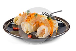 Three stuffed cabbage, decorated with carrots and hot pepper, lie on a black glossy plate with a black fork, isolated on