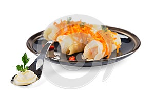 Three stuffed cabbage, decorated with carrots and hot pepper, lie on a black glossy plate with a spoon with sour cream
