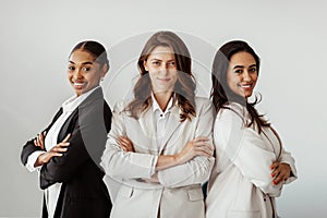 Three successful multicultural businesswomen standing with arms crossed and smiling at camera, posing in office