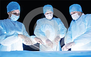 Three surgeons, a man and a woman, perform surgery in the operating room to remove and transplant human organs, resect