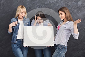 Three surprised girlfriends holding blank white banner