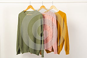 Three sweaters hanging from clothes rail with copy space on white background