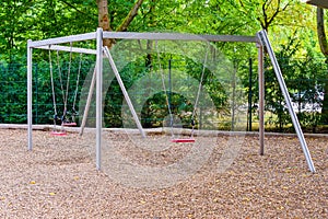 Three swings with metal chains and poles on a public playground