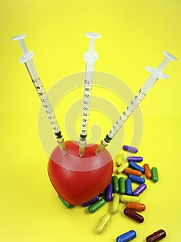 Three syringes pined to a red spongy heart with pills