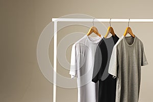 Three t shirts on hangers hanging from clothes rail and copy space on grey background