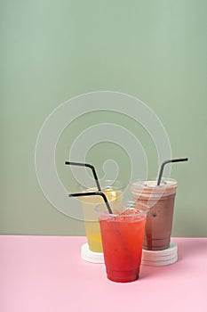 Three takeaway glasses of colourful summer drinks. Lemonades and cocktail on coloured background