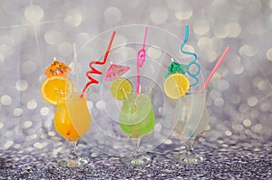 Three tall glasses with orange, lemon and lime juice on a gray background, decorated with citrus slices