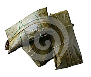 Three tamales wrapped in banana leaf on white background