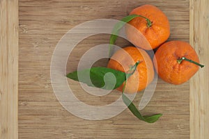 Three tangerines with leaves on wooden board