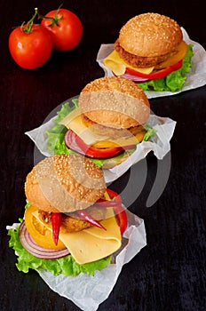 Three tasty burgers with falafel, salad, onion rings, cheese, tomatoes and chili pepper on the black background