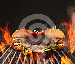 Three tasty hamburgers with beef, lettuce, cheese and spicy red pepper roasted on metal portable barbecue BBQ grill with