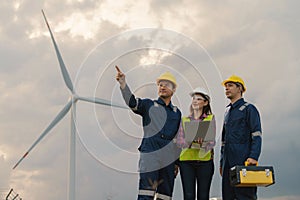 Three technician engineer in uniform with standing and checking wind turbine power farm power generator Station. Clean energy and