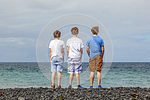 Three teen boys stand at a black volcanic beach