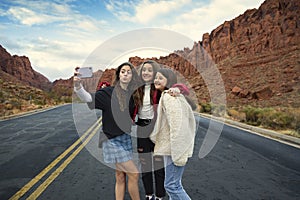 Three teen girls taking a selfie photo together outdoors with beautiful scenic red cliffs in the background.