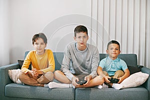 Three of the teen`s best happy friends are playing a video game at home. Three brothers play a video game, sitting on the couch,
