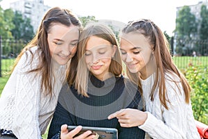 Three teenage girls of 12-14 years old, summer city watching videos phone, happy smiling people having fun rejoice