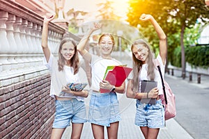 Three teenage girls (14-15 years old) walk to school, holding books and notebooks