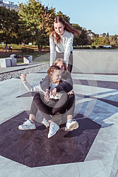 Three teenage girls of schoolgirls 12-14 years old, in summer in city, ride skateboard, happy smiling, having fun