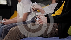 Three teenagers with joysticks play video games on the console sitting on a sofa