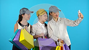 Three teenagers make selfies with colorful packages. Blue background