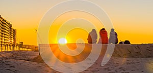 Three teenagers sitting on a sand hill together, watching and enjoying the sunset at the beach, young people in nature