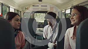 Three teenagers sitting school bus talking alone. Smiling girl taking seat.