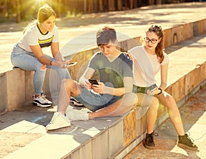 Three teenagers with smartphones are talking about play on walk