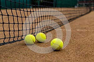 Three tennis balls lie side by side on a red clay court along the playing net