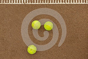 Three tennis balls lie side by side on a red clay court along. View from above