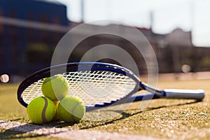 Three tennis balls and racket on hard court
