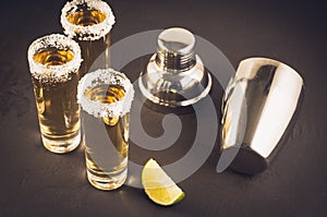 Three Tequila shot with lime fruit and shaker/three Tequila shot with lime fruit and shaker on a dark background. Selective focus