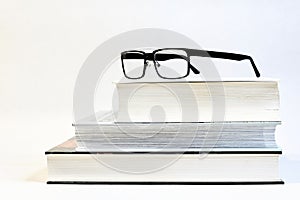 Three thick books on a table with glasses and a white background