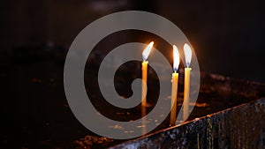 Three thin candles are burning in the dark interior of the church with somber and spiritual ambience