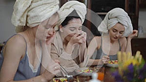 Three thoughtful young women with towels on their heads are having breakfast sitting at a table in the living room