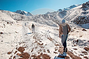 Three tourists on the mountain trail climb the snow top