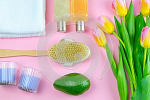 Three towels, body care oils, avocado and a tulips stand on a pinc background. The concept of spa treatments, a healthy body
