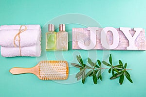 Three towels, body care oils, a green branch and a sprout with a joy sign stand on a green background. The concept of spa