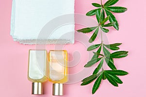 Three towels, body care oils and a green branch stand on a green background. The concept of spa treatments, a healthy body