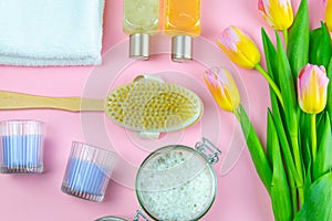 Three towels, body care oils and a tulips stand on a pinc background. The concept of spa treatments, a healthy body