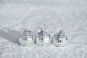 Three toy mirror disco balls lie on natural snow. Winter Christmas and New Year background. Frosty weather with loose snowy