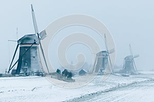 Three traditional Dutch windmills in the snow during blue hour