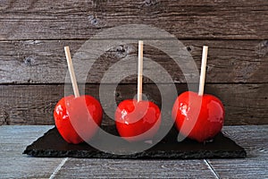 Three traditional red candy apples against a rustic wood background